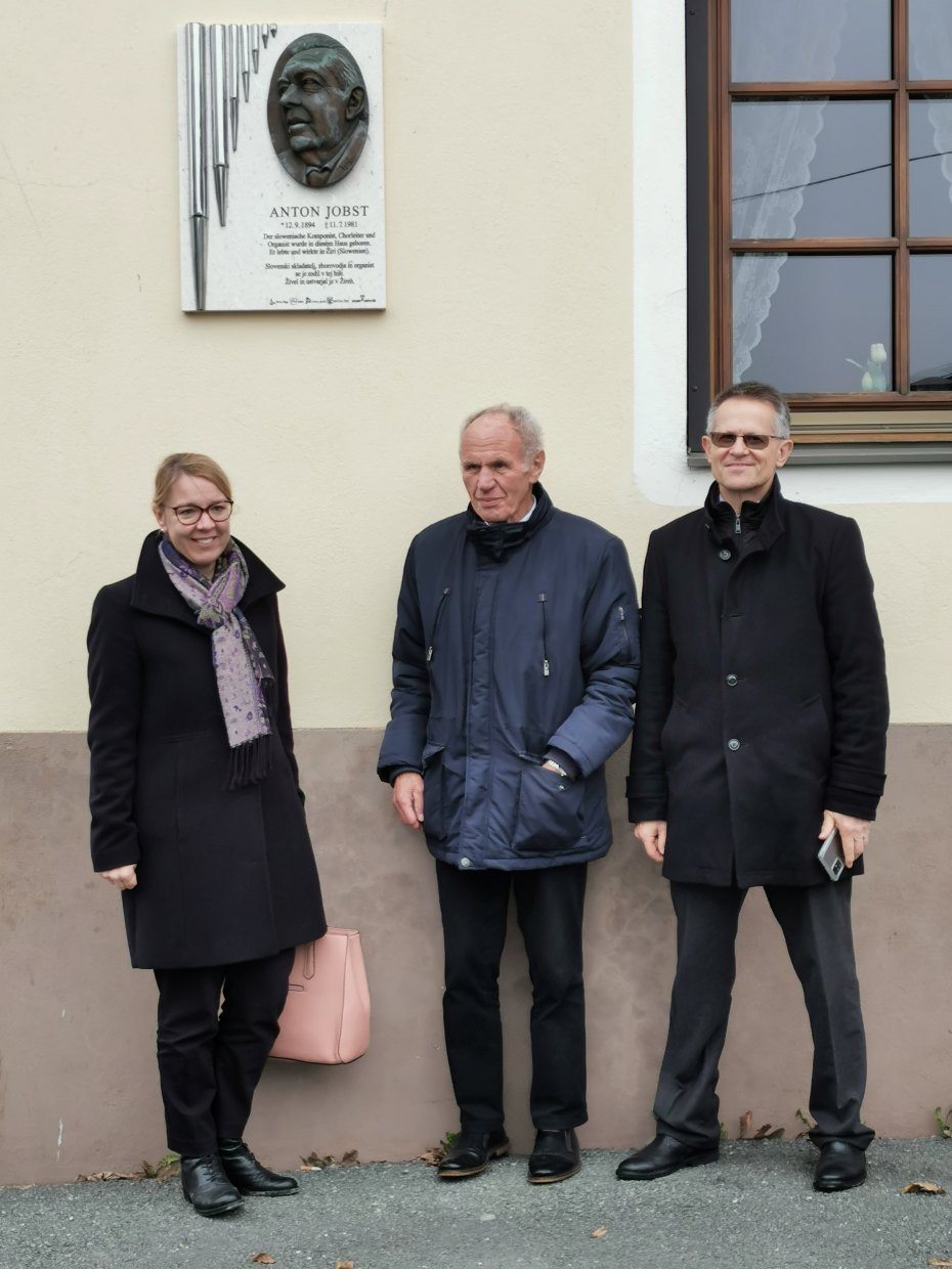 Image: Ministrica, župnik in generalni konzul pred spominsko ploščo Antonu Jobstu na njegovi rojstni hiši na Brdu. Foto: Franc Wakounig